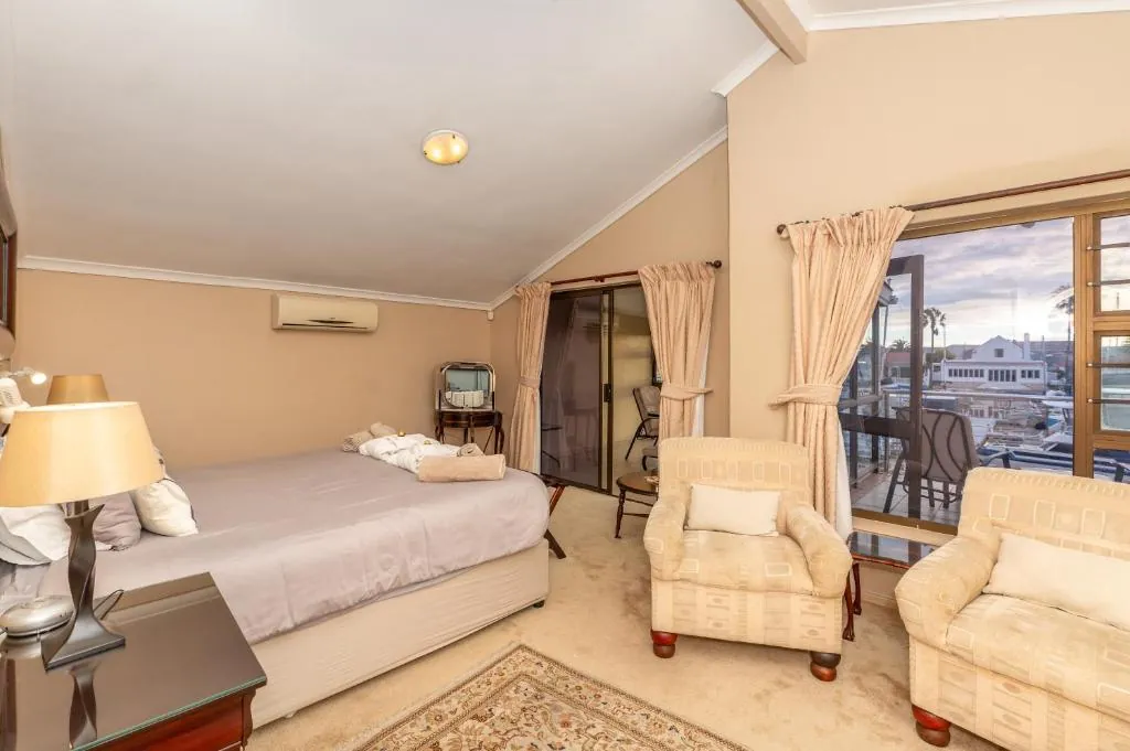 King bedroom with armchairs and sliding doors onto a balcony over the marina